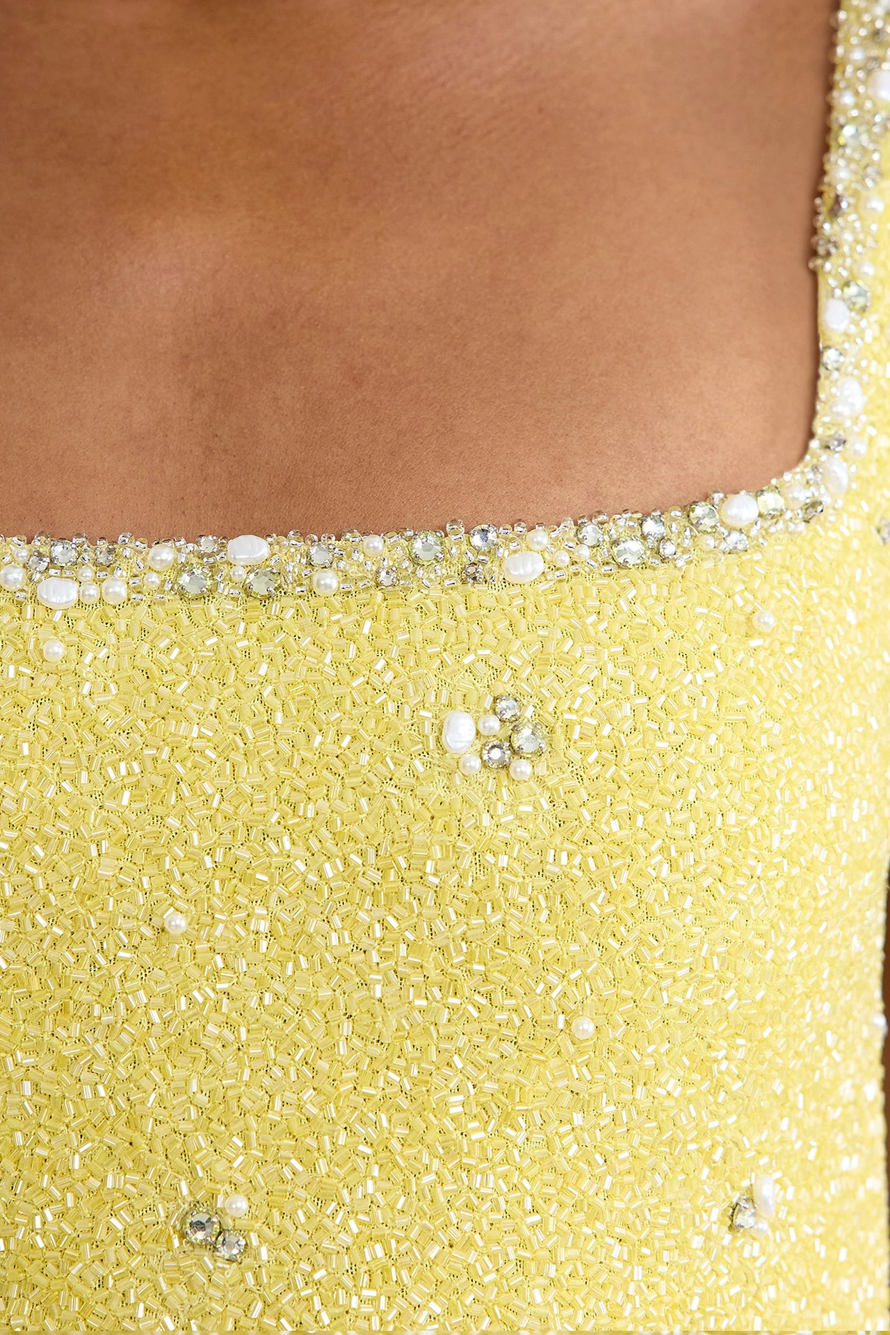 Close-up of square neck dress with pearls and shiny crystals on yellow fabric