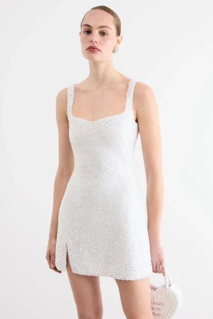 Ivory bridal shower mini dress worn by model with sweetheart neckline and split hem next to heart bag.