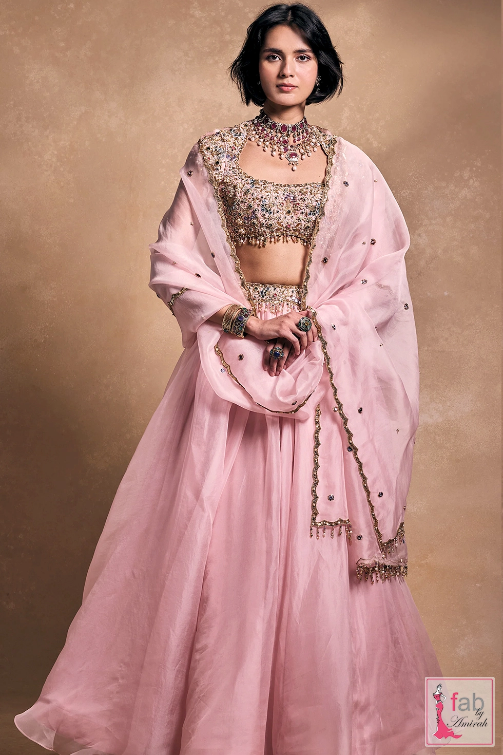 Model wearing baby pink embroidered lehenga set in studio setting Model wearing baby pink embroidered lehenga set in studio setting