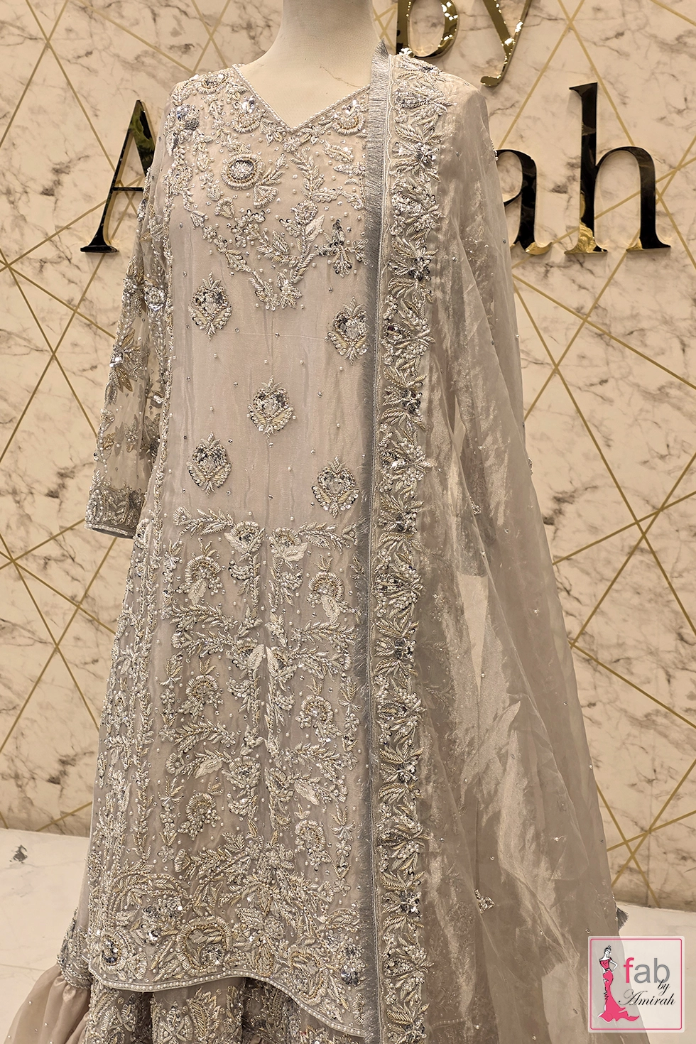Silver gharara suit displayed on mannequin with hand embroidered dupatta frame