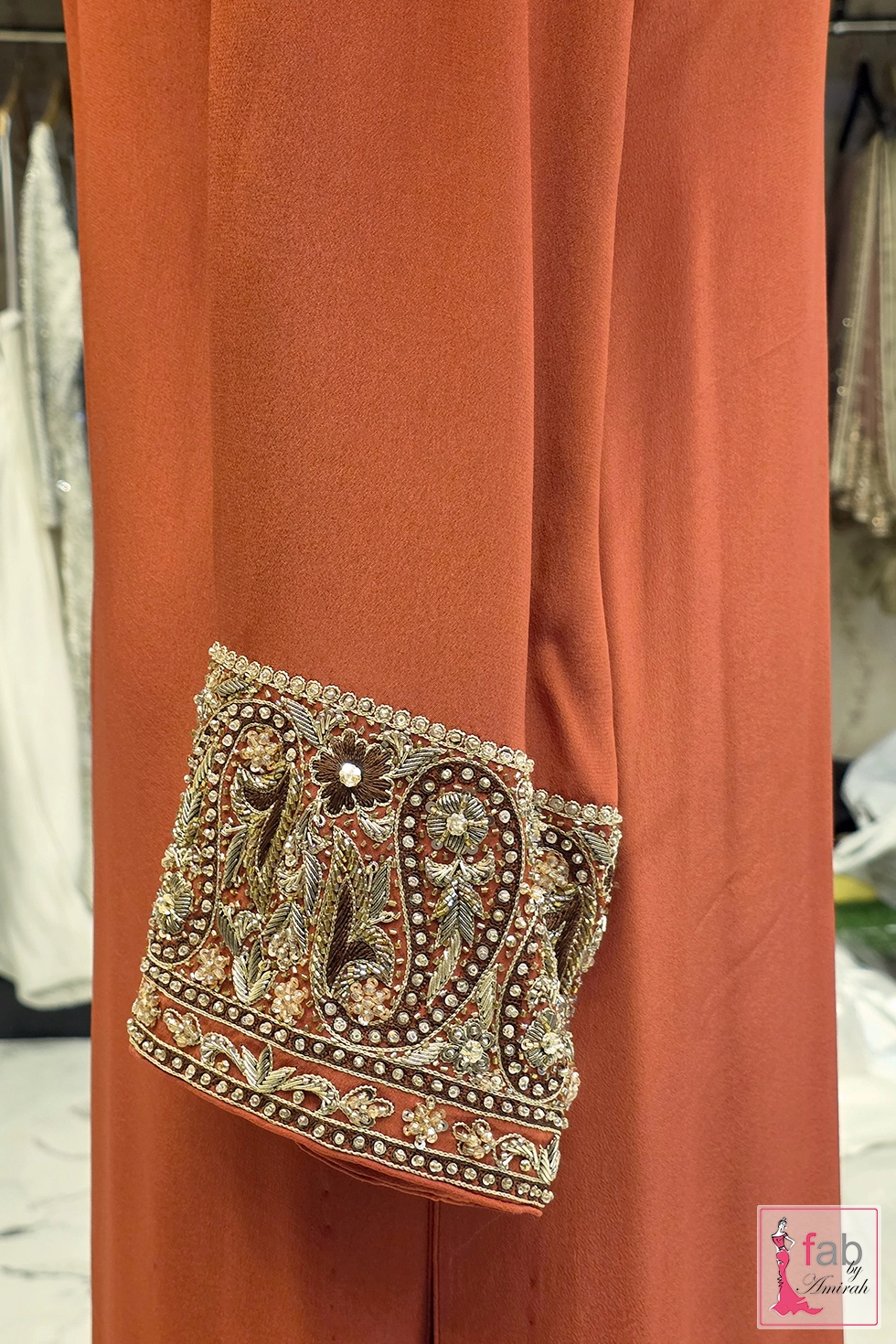 Detailed view of hand embroidered cuff on rust long sleeve shirt