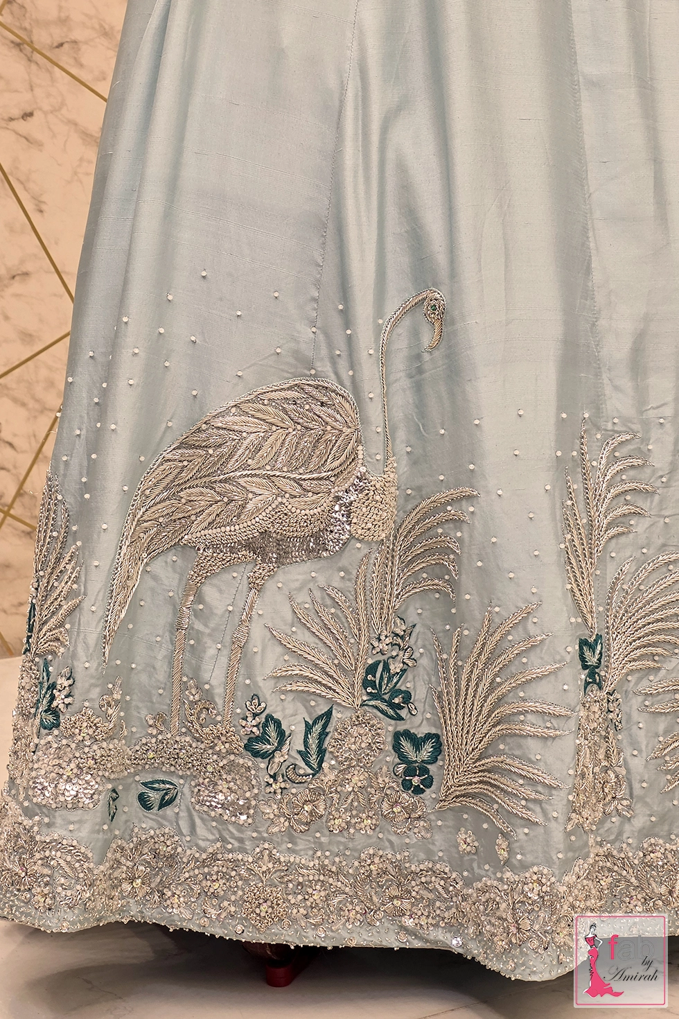 Close up view of detailed hand embroidered crane motif and pearl spray on ice blue fabric