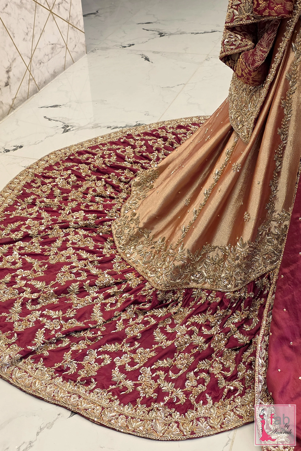 Back angle detail view of maroon farshi lehenga train spread with dense gold floral handwork.
